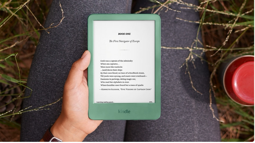 Kindle Basic color matcha sostenido en una mano, leyendo al aire libre sobre el pasto