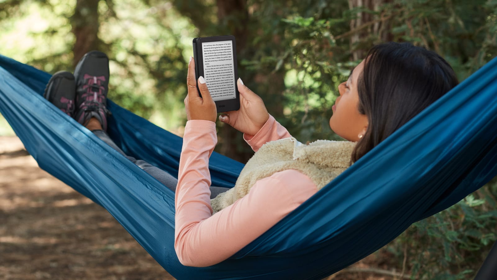 Mujer leyendo en su Kindle Basic recostada en una hamaca en el bosque