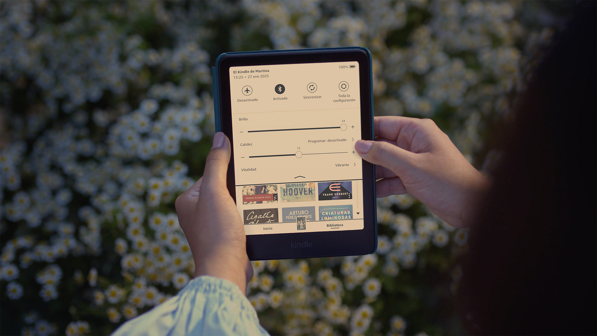 Manos ajustando brillo y calidez en el menú en español del Kindle Colorsoft, frente a un jardín de flores