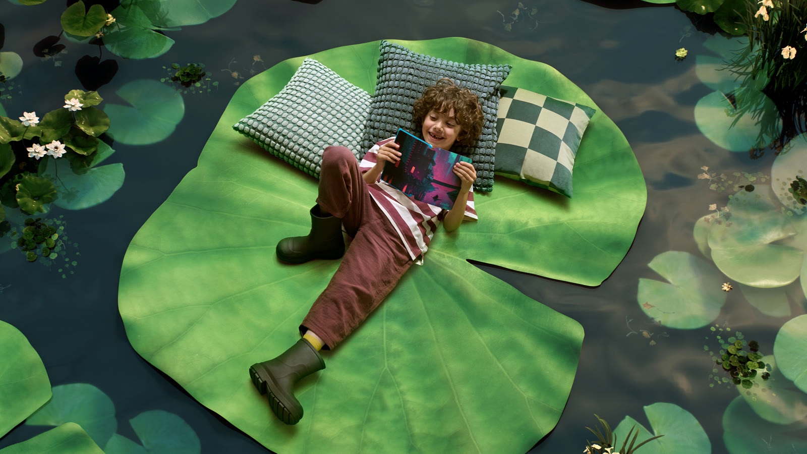 Niño leyendo un Kindle Paperwhite Kids recostado sobre una hoja de nenúfar gigante
